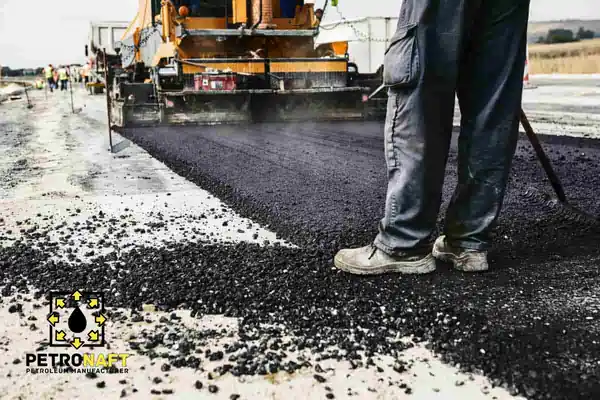 The roller is building the road and the worker is standing on the side of the road